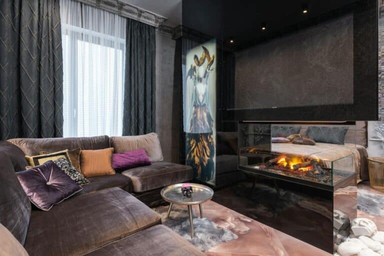 Interior of modern cozy apartment with comfortable sofa placed near contemporary burning firewood in room with bed at stylish home